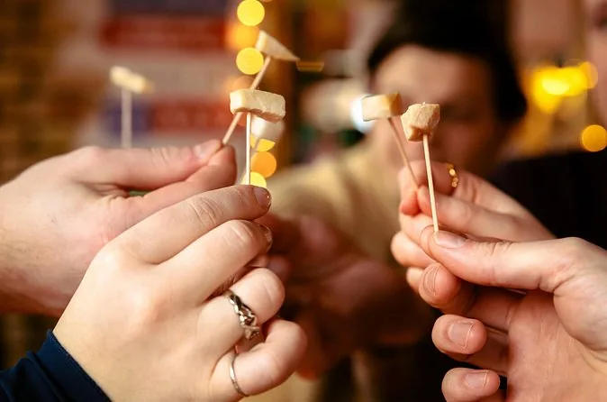 Diverse mani che sollevano piccoli cubetti bianchi su stuzzicadenti in un bar caldo e poco illuminato